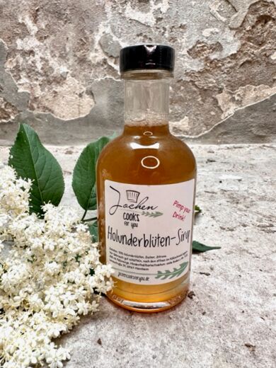 Holunderblüten Sirup in der Flasche mit Schraubverschluss und Blüten als Deko.